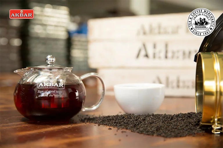 Akbar Ceylon Tea in a glass teapot with loose black tea and packaging crates – premium Sri Lankan tea by Akbar Brothers.